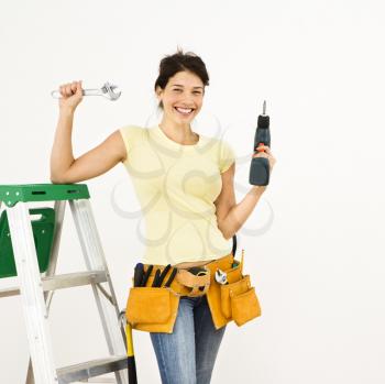 Royalty Free Photo of a Woman Standing in a Home With a Ladder and Holding Tools Smiling