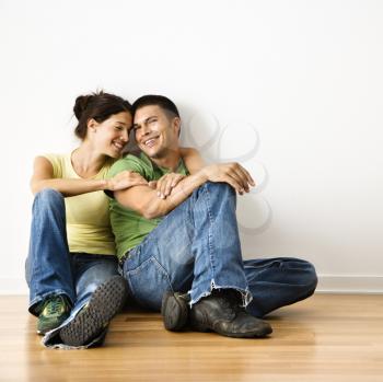 Royalty Free Photo of a Couple Sitting Together on Hardwood Floor at Home Smiling