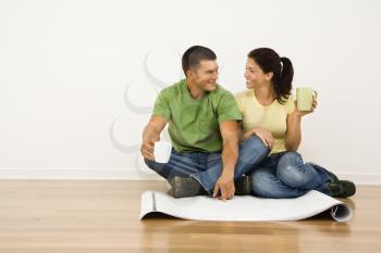 Royalty Free Photo of an Attractive Couple Sitting on Home Floor With Coffee Cups Looking at House Plans and Smiling