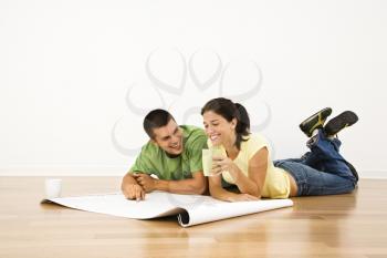 Royalty Free Photo of a Couple Lying on a Home Floor With Coffee Cups Smiling and Looking at Blueprints