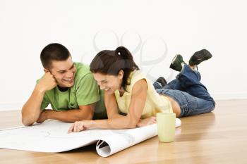 Royalty Free Photo of a Couple Lying on a Home Floor With Coffee Cups Smiling and Looking at Blueprints