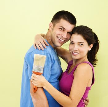 Happy smiling couple holding paintbrush in front of freshly painted interior wall.