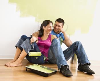 Royalty Free Photo of a Couple Sitting on the Floor Smiling in Front of a Partially Painted Wall in Home