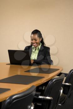 Royalty Free Photo of a Businesswoman Sitting at a Conference Table Smiling and Typing on a Laptop Computer