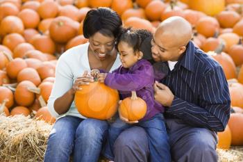 Royalty Free Photo of Parents and Their Daughter Picking Out a Pumpkin and Smiling at an Outdoor Market