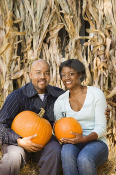 Royalty Free Photo of a Happy Smiling Couple Sitting on Hay Bales and Holding Pumpkins at an Outdoor Market