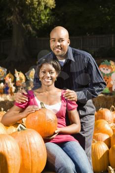 Portrait of happy smiling couple sitting in pumpkins at outdoor market.