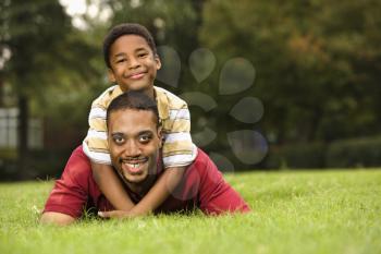 Royalty Free Photo of a Father Lying in the Grass While His Son Climbs on His Back