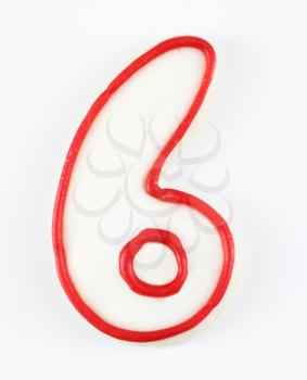 Sugar cookie in the shape of a number six outlined in red icing.