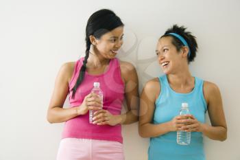 Royalty Free Photo of Two Young Women in Fitness Clothes Holding Water Bottles Standing Smiling and Talking