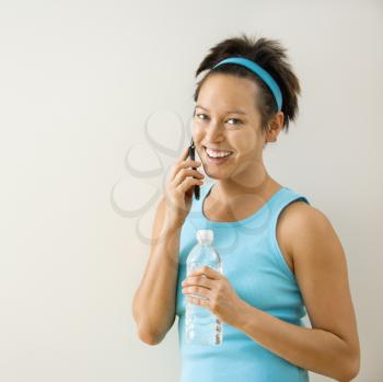 Royalty Free Photo of a Woman in Fitness Clothing Holding Bottled Water and Talking on a Cellphone