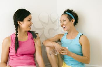 Royalty Free Photo of Two Young Women in Fitness Clothes Holding Water Bottles Sitting Smiling and Talking