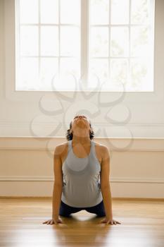 Young woman doing yoga cobra pose on wooden floor indoors by sunlit window.
