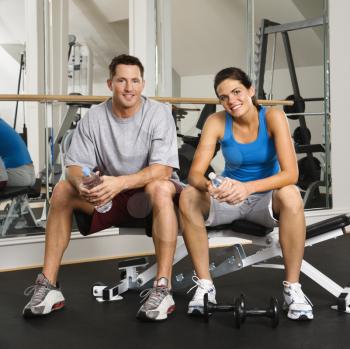 Royalty Free Photo of a Man and Woman Sitting on an Exercise Machine Holding Water Bottles