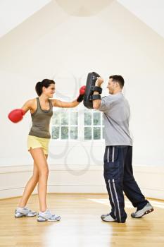 Royalty Free Photo of a Woman Wearing Boxing Gloves Hitting Training Mitts a Man is Holding