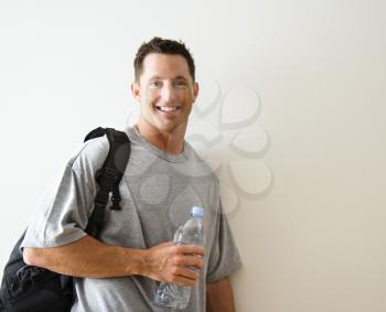 Man standing smiling with gym bag and bottled water.