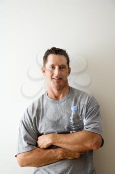 Head and shoulder portrait of man in t-shirt against white wall holding water bottle and smiling.
