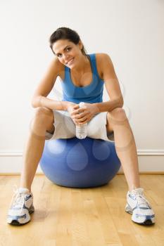 Royalty Free Photo of a Woman Holding a Water Bottle Sitting on a Balance Ball at a Gym Smiling
