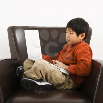 Royalty Free Photo of a Boy With a Laptop Computer Sitting in a Chair