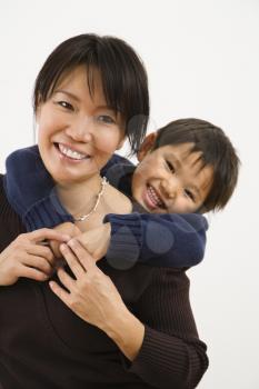 Royalty Free Photo of an Asian mother with young son hugging her from behind smiling