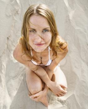 Royalty Free Photo of a Redheaded Woman Sitting on a Beach Wearing a Bikini