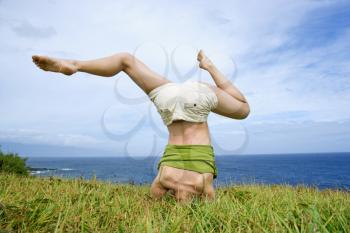 Royalty Free Photo of a Young Woman Doing a Headstand With Legs Askew in Grass Near Ocean in Maui, Hawaii