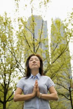 Royalty Free Photo of a Woman Standing Outside Meditating With Skyscrapers Behind Her