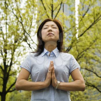 Royalty Free Photo of a Woman Standing Outside With trees and Skyscrapers Behind Her Meditating