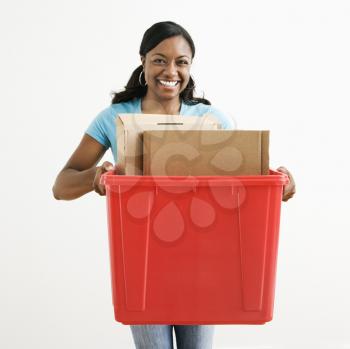 African American young adult female holding recycling bin with cardboard in it.