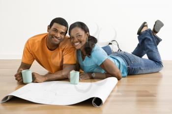 African American male and female couple with architectural  blueprints drinking coffee.