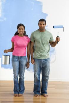 Royalty Free Photo of a Couple Standing Next to a Half-Painted Wall with Paint Supplies - American Gothic-Style