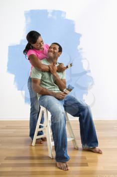 Portrait of African American male and female couple next to half-painted wall.
