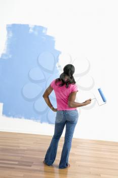 Royalty Free Photo of a Woman Standing Next to a Half-Painted Wall With a Paint Roller