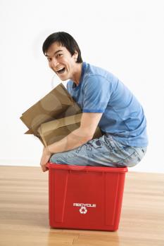Royalty Free Photo of a Man Trying to Sit in a Recycling Bin With Cardboard