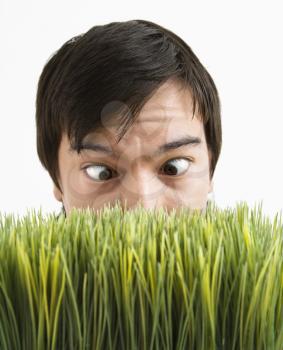 Asian young man looking over grass with eyes crossed.
