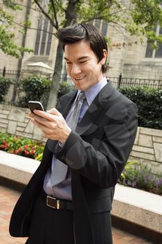 Asian business man standing looking at cell phone messages smiling.