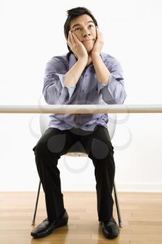 Royalty Free Photo of a Young Asian Businessman Sitting at a Desk Daydreaming