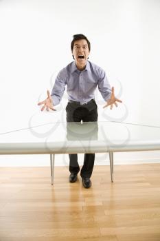 Young Asian business man standing at conference table yelling at unseen person.