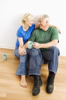 Royalty Free Photo of a Middle-aged Couple Sitting on the Floor Snuggling and Drinking Coffee