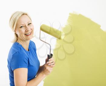 Royalty Free Photo of a Middle-aged Woman Painting a Wall Green With a Paint Roller and Smiling