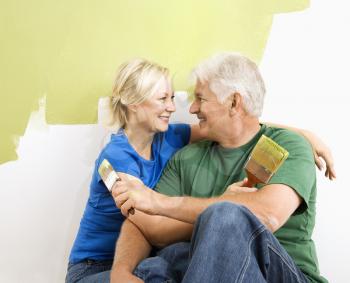 Royalty Free Photo of a Couple Sitting in Front of a Half-Painted Wall with Paint Supplies Hugging