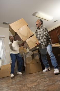 Senior african american man dropping stacked moving boxes while his wife attempts to catch them.