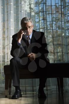 Businessman in suit with serious expression sitting talking on a mobile phone. Vertical shot.
