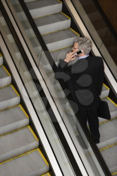 Businessman has a mobile phone conversation while riding the escalator. Vertical shot.