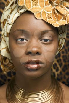 Close-up portrait of an African American woman wearing traditional African clothing in front of a patterned wall. Vertical format.