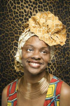 Close-up portrait of a smiling African American woman wearing traditional African clothing in front of a patterned wall. Vertical format.