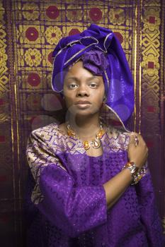 Portrait of an African American woman wearing traditional African clothing in front of a patterned wall. Vertical format.