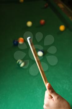 Hand holding a pool cue with a billiards table in background. Vertical shot.