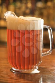 Full beer pitcher with foam on a bar counter. Vertical shot.