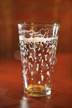 Empty beer glass on bar counter with residual foam lining the glass. Vertical shot.
